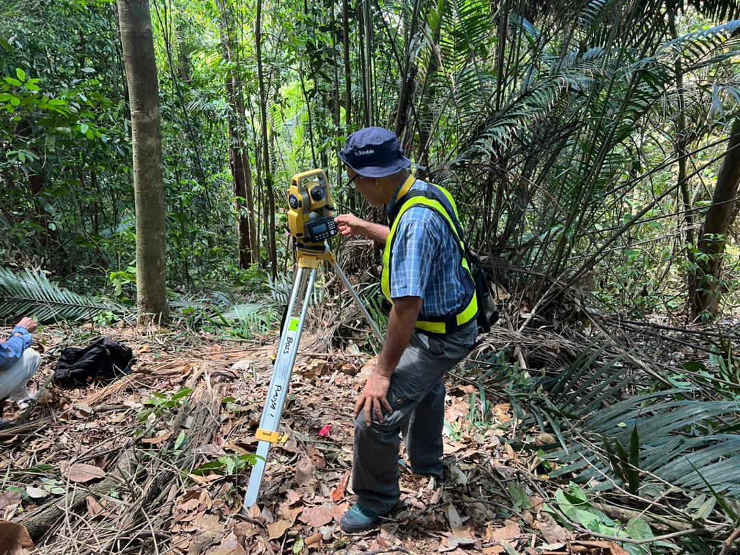 Surveyor operating a total station in wooded terrain